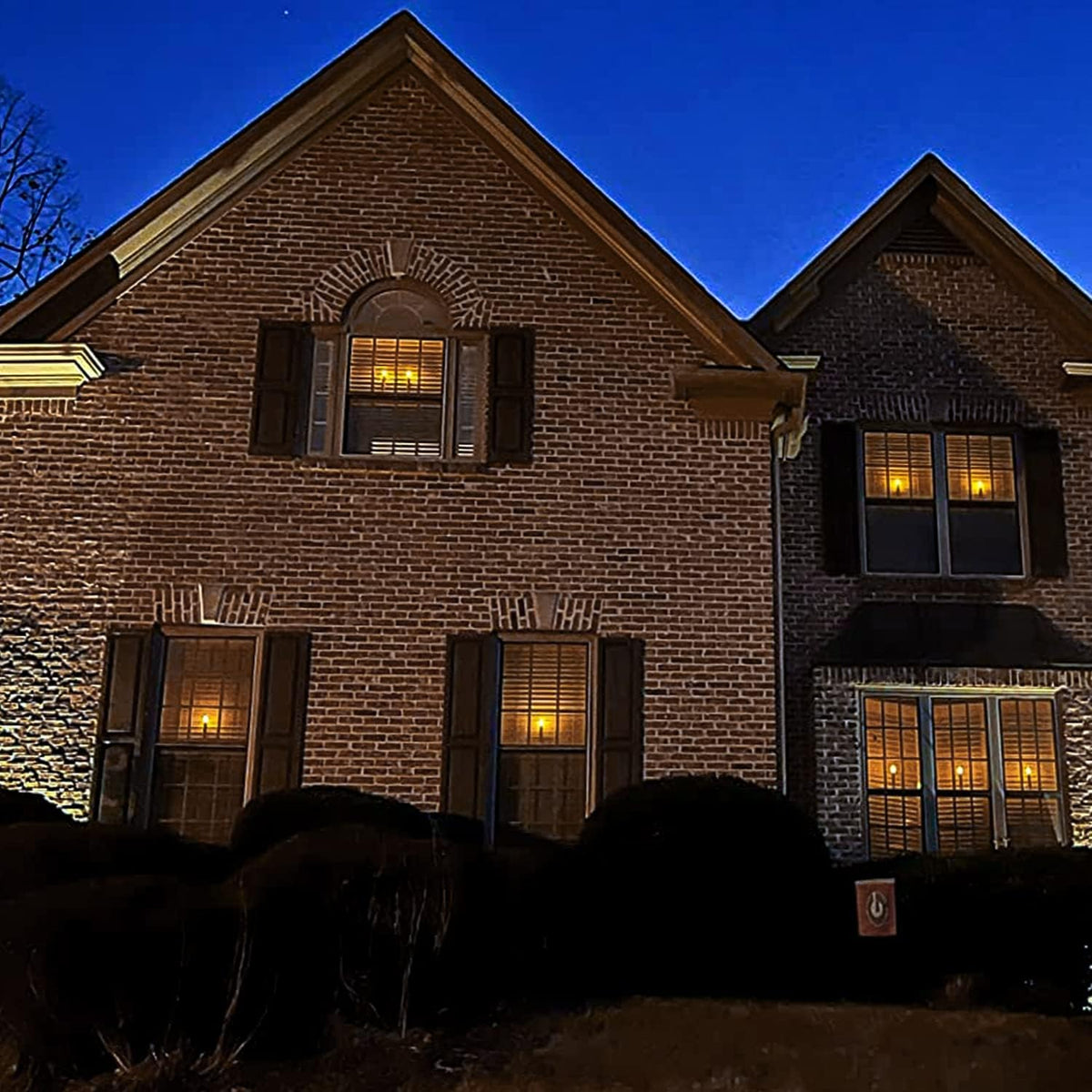 A brick home with coordinated glowing window candles at night